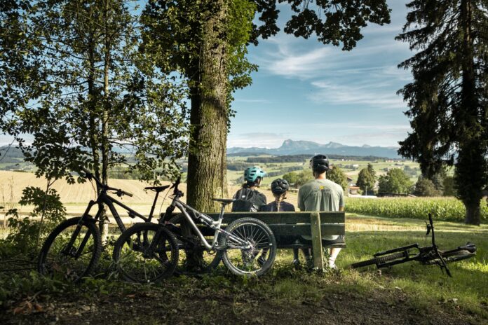 Familie mit Kinderbikes macht Pause auf einer Bank in Lussy bei Romont Familie mit Kinderbikes macht Pause auf einer Bank in Lussy bei Romont