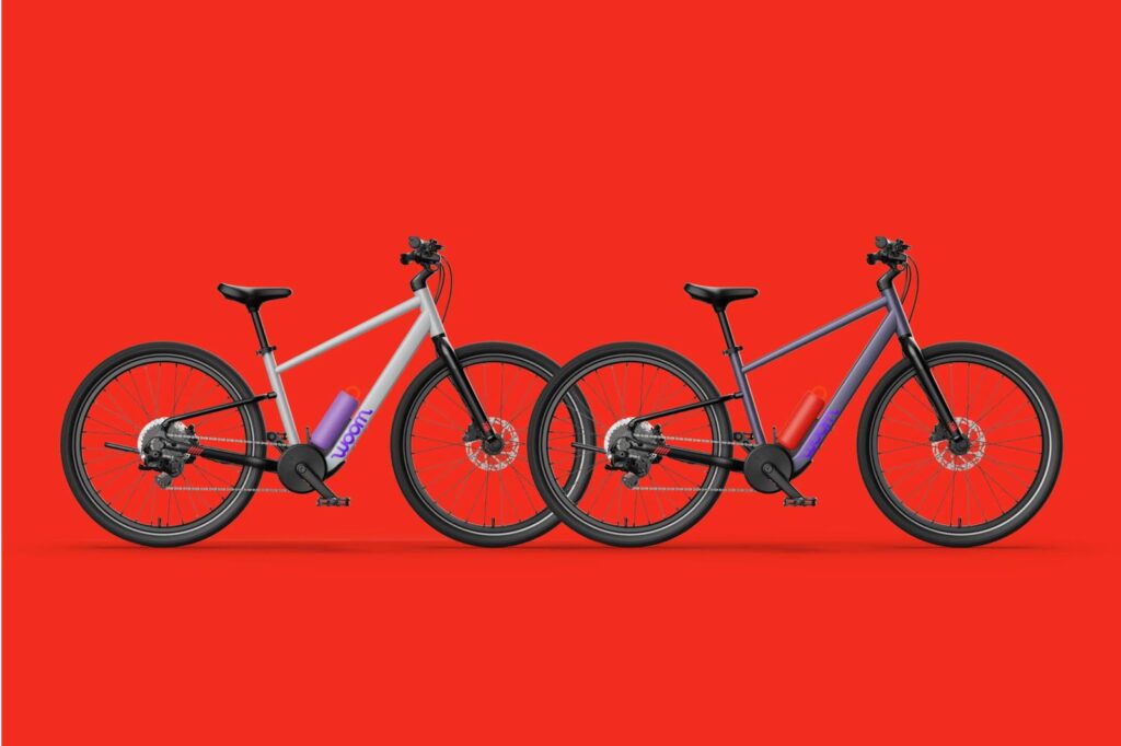 Zwei woom EXPLORE BOOST Kinder-E-Bikes vor rotem Hintergrund